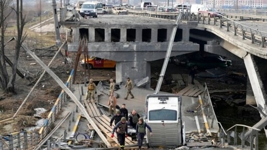 Ukrainian soldiers carry a body of a civilian killed by the Russian forces over the destroyed bridge in Irpin close to Kyiv, Ukraine.(AP)