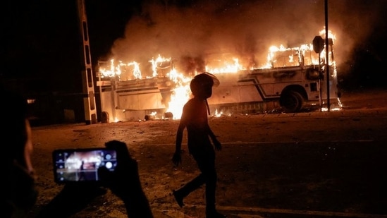 A person takes a photo as a demonstrator walks near a bus that was set on fire at the top of the road to Sri Lankan President Gotabaya Rajapaksa's residence during a protest against him.(REUTERS/Dinuka Liyanawatte)