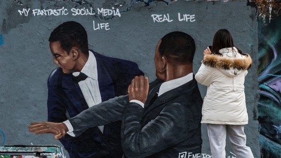 A woman takes a photo of a mural by Berlin-based street artist Eme Freethinker featuring the likeness of US actor Will Smith (R) slapping US comedian Chris Rock during the Oscars ceremony, in Berlin.(AFP)