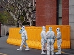 Workers in protective suits stand next to a sealed-off area before the second stage of a two-stage lockdown to curb the spread of COVID-19, in Shanghai