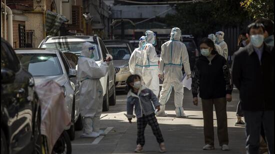 Workers in personal protective equipment (PPE) keep watch as residents queue for a Covid-19 test in a neighbourhood placed under lockdown in Shanghai, China, on Monday. (Bloomberg)