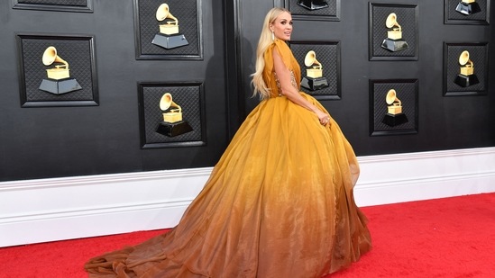 Carrie Underwood arrived for the 64th Annual Grammy Awards at the MGM Grand Garden Arena in a Princess-esque gown replete with mustard and brown shades. She teamed it with minimal make-up and striking jewels.(AFP)