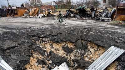 A local resident rides a bicycle past a bomb crater, as Russia's attack on Ukraine continues, in the village of Demydiv, outside Kyiv, Ukraine. (REUTERS)