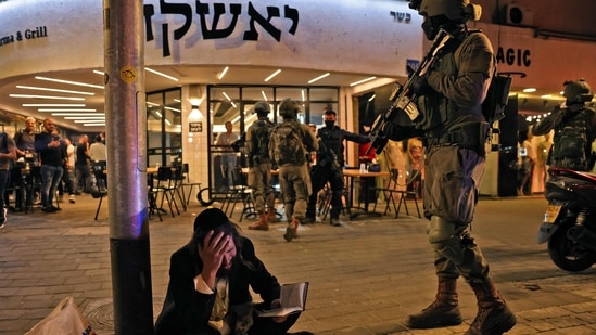 An ultra-Orthodox Jewish man reacts while holding a volume of the Book of Psalms while security forces gather behind at the scene of a shooting attack in Dizengoff Street in the centre of Israel's Mediterranean coastal city of Tel Aviv. (AFP)