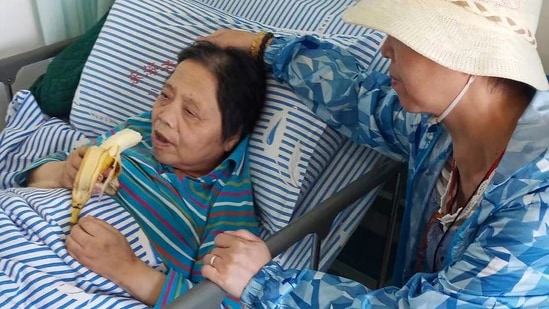 Shen Peiming, 71, eats a banana as a family member attends to her at a Shanghai hospital in 2019. Shen died on Sunday morning,&nbsp;(AP)