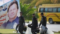 Security personnel walk past a banner featuring an image of Pakistan's Prime Minister Imran Khan near Parliament House building in Islamabad.&nbsp;