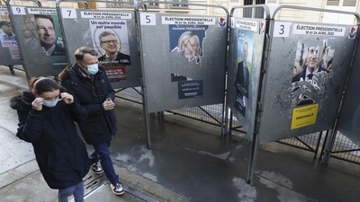 People wearing protective face masks walk past bulletin boards with official campaign posters of French presidential election candidates near a polling station, during the first round of the 2022 French presidential election, in Paris, France.&nbsp; (REUTERS)