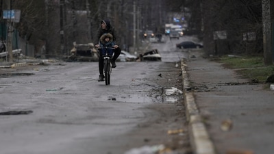 A man and child ride on a bicycle as bodies of civilians lie in the street in the formerly Russian-occupied Kyiv suburb of Bucha, Ukraine. (AP) A man and child ride on a bicycle as bodies of civilians lie in the street in the formerly Russian-occupied Kyiv suburb of Bucha, Ukraine. (AP)