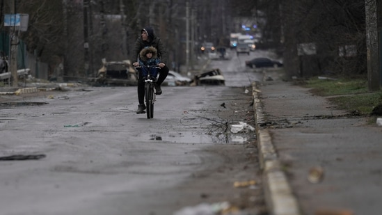 A man and child ride on a bicycle as bodies of civilians lie in the street in the formerly Russian-occupied Kyiv suburb of Bucha, Ukraine.(AP)