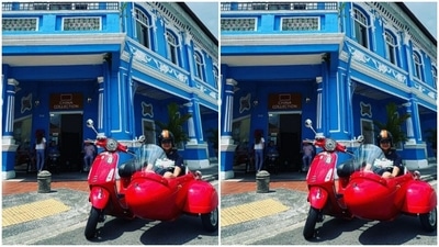 Here's a picture of Gul posing in the red motorcycle with sidecar against a bright blue building in Singapore. (Instagram/@gulpanag)