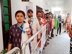A security person stands guard as electors wait for their turn to cast their vote in the Uttar Pradesh Legislative Council elections. (PTI PHOTO)