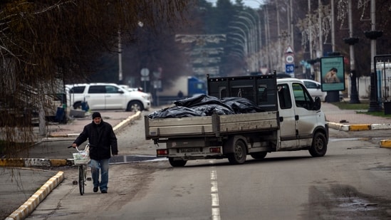 A man walks with a bicycle next to a truck that carries black bags with corpses of people killed during the war with Russia and exhumed from a mass grave for investigations in Bucha, on the outskirts of Kyiv, Ukraine, Monday.&nbsp;