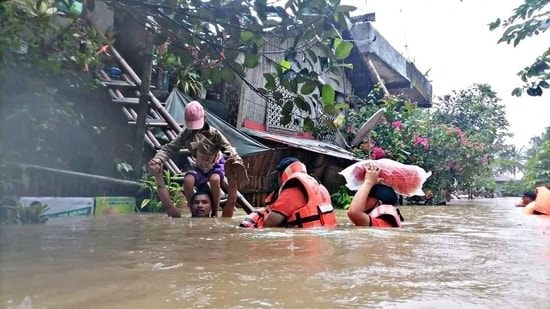 A man carries a boy on his shoulder as they walk through a flooded road along with rescue personnel, after the tropical storm Megi hit, in Capiz Province, Philippines April 12, 2022. (Philippine Coast Guard/Handout via REUTERS)
