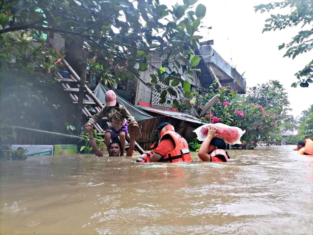 A man carries a boy on his shoulder as they walk through a flooded road along with rescue personnel, after the tropical storm Megi hit, in Capiz Province, Philippines April 12, 2022. (Philippine Coast Guard/Handout via REUTERS)