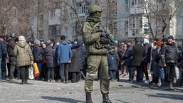 A Russian army soldier stands next to local residents who queue for humanitarian aid delivered during Ukraine-Russia conflict, in the besieged southern port of Mariupol, Ukraine.