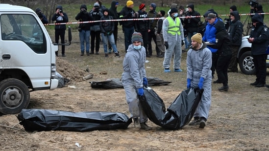 Journalists gather as bodies are exhumed and removed from a mass grave in the Ukrainian town of Bucha.(AFP)