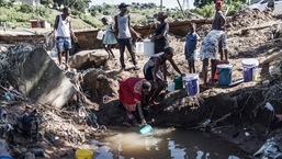 Men gesture while women fill buckets with water from a stream in the Inanda district of Durban, on April 15, 2022, near a waterfall created by a collapsed road. &nbsp;(Photo by MARCO LONGARI / AFP)