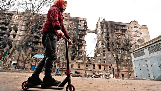 A boy rides a scooter near a building destroyed during Ukraine-Russia conflict in the southern port city of Mariupol. REUTERS