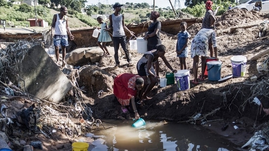 Men gesture while women fill buckets with water from a stream in the Inanda district of Durban, on April 15, 2022, near a waterfall created by a collapsed road. &nbsp;(Photo by MARCO LONGARI / AFP)(AFP)