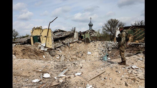 A Ukranian serviceman looks into a crater and a destroyed home are pictured in the village of Yatskivka, eastern Ukraine on April 16, 2022 (AFP)