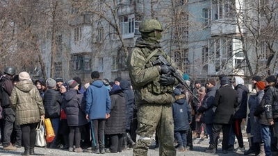A Russian army soldier stands next to local residents who queue for humanitarian aid delivered during Ukraine-Russia conflict, in the besieged southern port of Mariupol, Ukraine. (REUTERS)