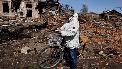 An elderly woman takes notes as she stands in front of her house, which according to her was destroyed by air missiles amid Russia's invasion of Ukraine, in Trostianets, Sumy region. (Reuters)