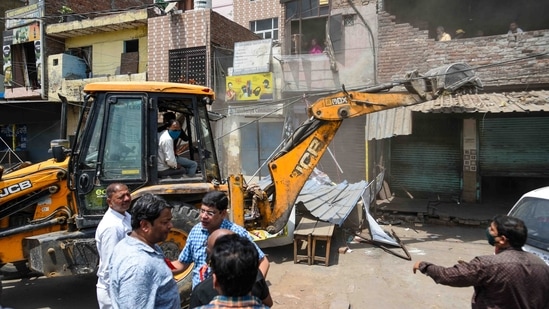 Local residents look on from their houses as a bulldozer demolishes an illegal structure during the anti-encroachment drive in Jahangirpuri, New Delhi, on April 20, 2022. "They razed my shop and took away four carts. This was the only source of income for our family of five. I have two kids and both are studying in primary schools. I am worried how their studies will continue and have lost all hopes for their good future. I am clueless about recovering our losses," resident Malika Bibi told PTI.(Amal KS / HT Photo)