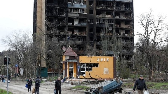 People walk past a residential building heavily damaged during Ukraine-Russia conflict in the southern port city of Mariupol, Ukraine(REUTERS)
