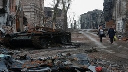 Guerra na Ucrânia: Pessoas caminham perto de um tanque destruído e prédios danificados durante o conflito Ucrânia-Rússia na cidade portuária de Mariupol, no sul, 