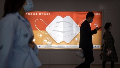 Commuters wearing face masks walk past a billboard encouraging people to wear masks in Beijing. (AP)