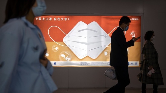 Commuters wearing face masks walk past a billboard encouraging people to wear masks in Beijing.(AP)