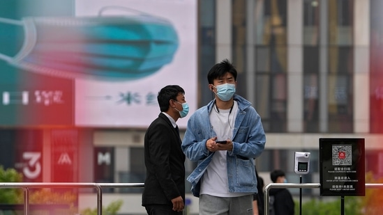 A man wearing a face mask walks by a masked security stands guard at a barricaded entrance displaying a health QR code and a temperature scanner at a commercial office complex, Sunday.(AP)