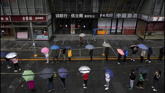 Locked-down residents line up in the rain for Covid test outside shuttered office complex in Beijing, on Wednesday. (AP)