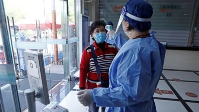 A worker in a protective suit measures the body temperature of a woman during a vaccination session against Covid-19 for elderly people, at a community health service centre in Fengxian district of Shanghai, China. (REUTERS) A worker in a protective suit measures the body temperature of a woman during a vaccination session against Covid-19 for elderly people, at a community health service centre in Fengxian district of Shanghai, China. (REUTERS)