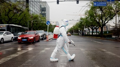 A worker wearing a protective suit and carrying disinfection equipment crosses a road amid the coronavirus disease (Covid-19) outbreak in Beijing, China. (REUTERS)