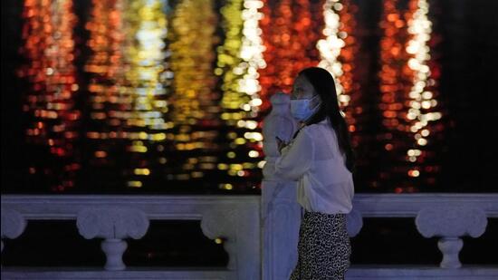 A resident wearing a mask walks past lights reflected from a river on Sunday, in Beijing. Many Chinese marked a quiet May Day this year as the government's "zero-Covid" approach restricts travel and enforces lockdowns in multiple cities. (AP)