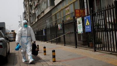 A worker in a protective suit carries disinfection equipment as he walks near an area under lockdown amid the coronavirus disease (COVID-19) outbreak in Beijing. (REUTERS)
