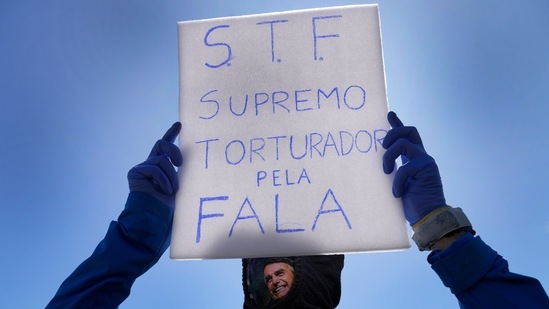 A man wearing a mask with the image of Brazil's President Jair Bolsonaro pasted on it holds a sign with text that reads in Portuguese "Supreme Court, supreme torturer for speech," during the Labour Day and Freedom rally in Brasilia, Brazil.(AP)