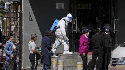 A worker in a protective suit sprays disinfectant as residents wearing face masks line up for mass coronavirus testing outside a residential complex, in Beijing, on Tuesday. (AP) A worker in a protective suit sprays disinfectant as residents wearing face masks line up for mass coronavirus testing outside a residential complex, in Beijing, on Tuesday. (AP)