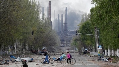 People walk their bikes across the street as smoke rises above a plant of Azovstal Iron and Steel Works during the Ukraine-Russia conflict in Mariupol,&nbsp; (REUTERS)