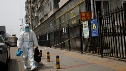 Um trabalhador em traje de proteção carrega equipamento de desinfecção enquanto caminha perto de uma área fechada em meio ao surto de doença por coronavírus (COVID-19) em Pequim.