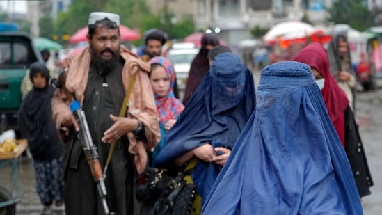 Women walk through the old market as a Taliban fighter stands guard, in the city of Kabul, Afghanistan,