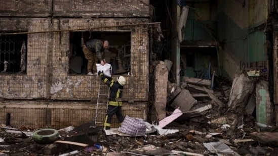 Um bombeiro ucraniano ajuda um homem a retirar pertences de um prédio destruído após ser atingido por um bombardeio de artilharia em Kiev. (AP)