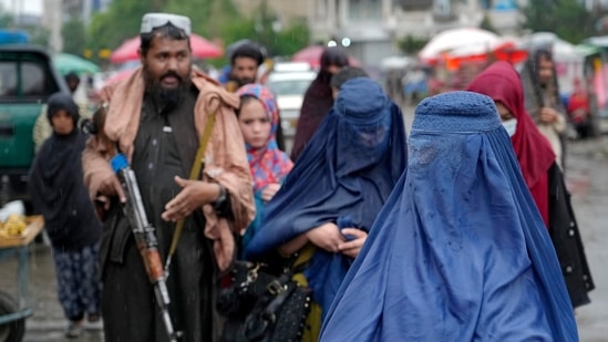 Women walk through the old market as a Taliban fighter stands guard, in the city of Kabul, Afghanistan,(AP)