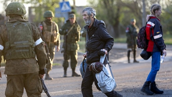 Um homem, que deixou um abrigo na Metalúrgica Combine Azovstal caminha para um ônibus entre militares do exército russo e milícia da República Popular de Donetsk em Mariupol. (AP)