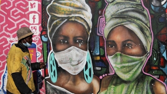 Um homem passa por um mural de Senzart911 que mostra pessoas usando máscaras em Kliptown, em Soweto, África do Sul. (Reuters)