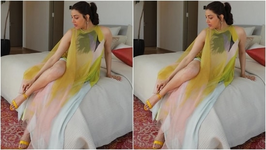 Kajal's dress comes from the shelves of clothing brand Payal Khandwala.  The sleeveless maxi outfit features a round neckline, a fitted silhouette accentuating Kajal's figure, a risque thigh-high slit to the side, and a tulle overlay in yellow and light pink ombre tones.  (Instagram/@kajalaggarwalofficial)