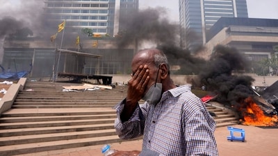 A Sri Lankan man reacts to tear gas as he walks past the vandalized site of anti-government protests outside president's office in Colombo, Sri Lanka, Monday, May 9, 2022.. (AP Photo/Eranga Jayawardena)