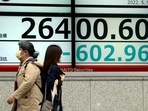 Women wearing protective masks walk in front of an electronic stock board showing Japan's Nikkei 225 index at a securities firm.