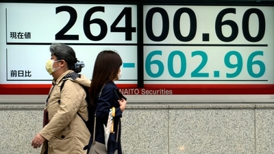 Women wearing protective masks walk in front of an electronic stock board showing Japan's Nikkei 225 index at a securities firm. (AP)